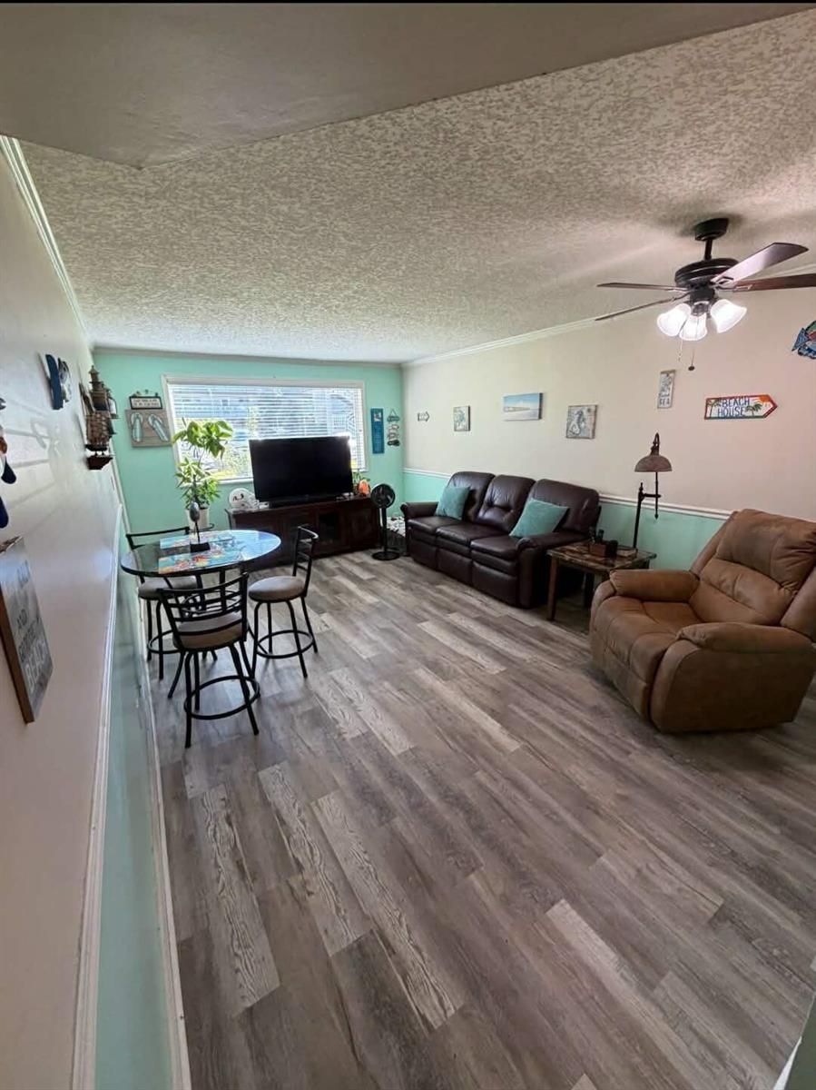 A living room with wood-look flooring, a brown leather sofa, a recliner, and a dining set — 2770 S Garden Drive # 107, FL 33461, FL