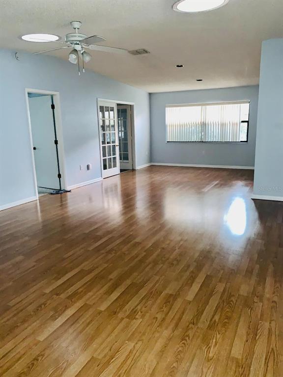 A spacious room with light blue walls, hardwood flooring, a ceiling fan, and French doors — 1846 MASTERS LANE, LAKELAND, FL