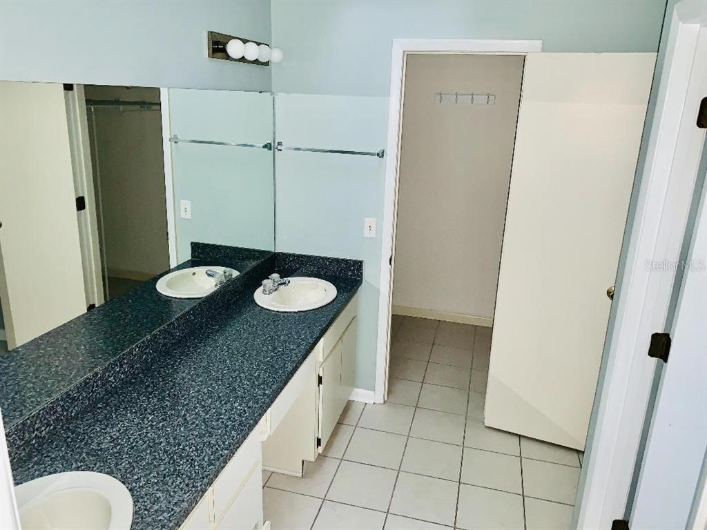 A bathroom features a dark speckled countertop, dual sinks, a large mirror, and tiled flooring — 1846 MASTERS LANE, LAKELAND, FL