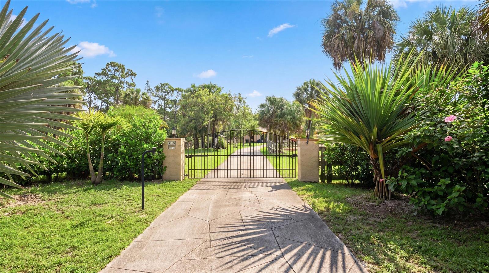 A paved driveway leads to a gated entrance surrounded by lush tropical landscaping and palm trees — 2910 Doe Trail, Loxahatchee FL 33470, LOXAHATCHEE, FL