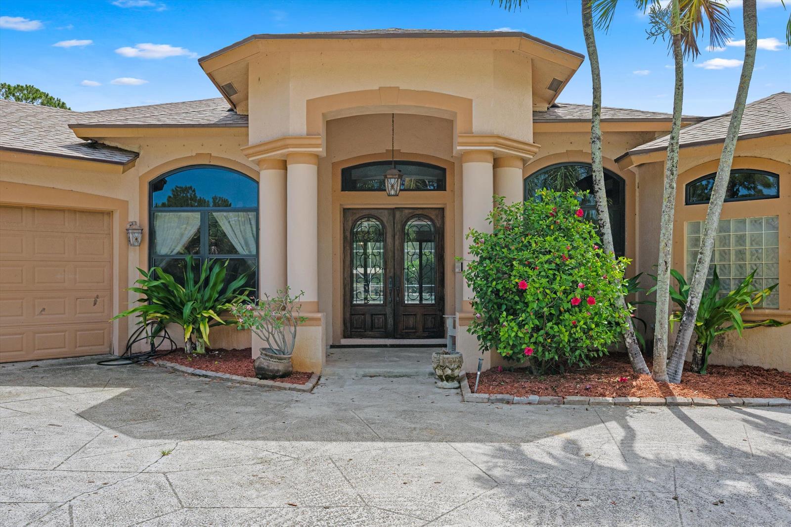The exterior of a beige house features a covered entryway with columns and double doors — 2910 Doe Trail, Loxahatchee FL 33470, LOXAHATCHEE, FL