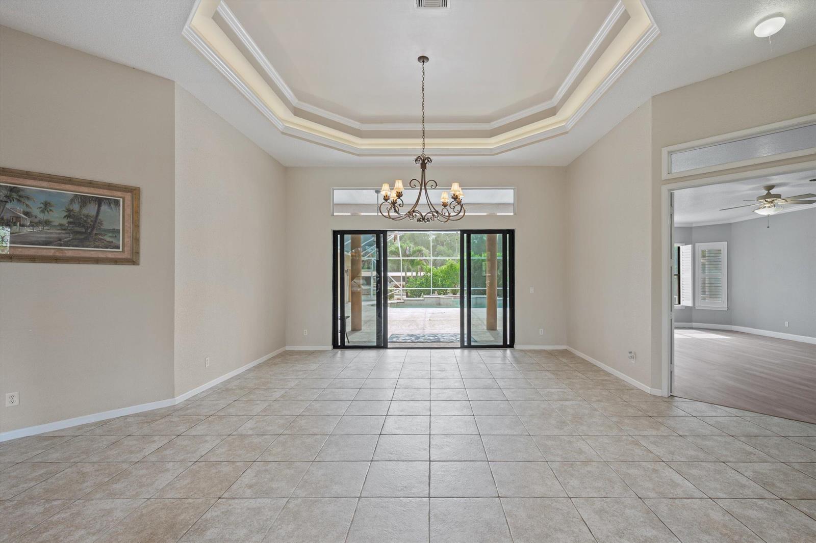 A dining room with a tray ceiling, chandelier, tile flooring, and sliding glass doors to a pool — 2910 Doe Trail, Loxahatchee FL 33470, LOXAHATCHEE, FL