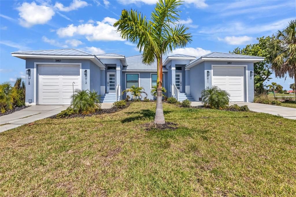 A blue duplex home features two garage doors, metal roofs, and a central palm tree — 3451 BAL HARBOR BOULEVARD, PUNTA GORDA, FL