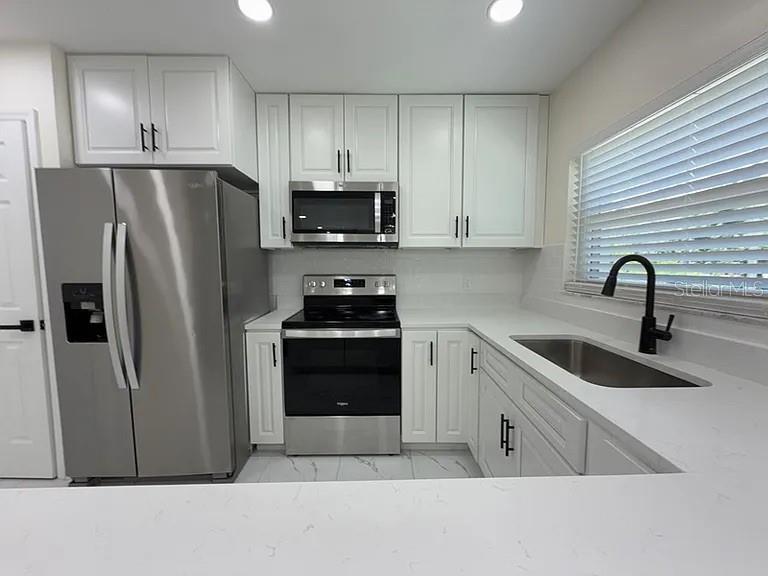 A kitchen featuring white cabinets, stainless steel appliances, a quartz countertop, and a black faucet — 270 W PINELOCH AVENUE, ORLANDO, FL