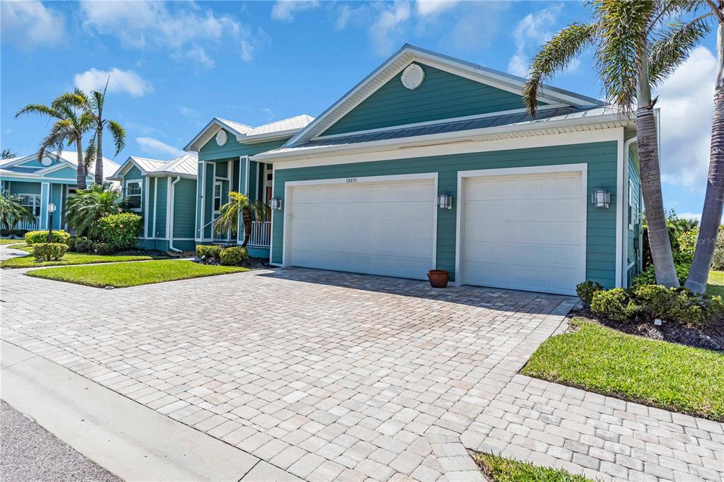 A teal house with a three-car garage and a paved driveway under a blue sky — 18091 WOODEN SKIFF COURT, NOKOMIS, FL