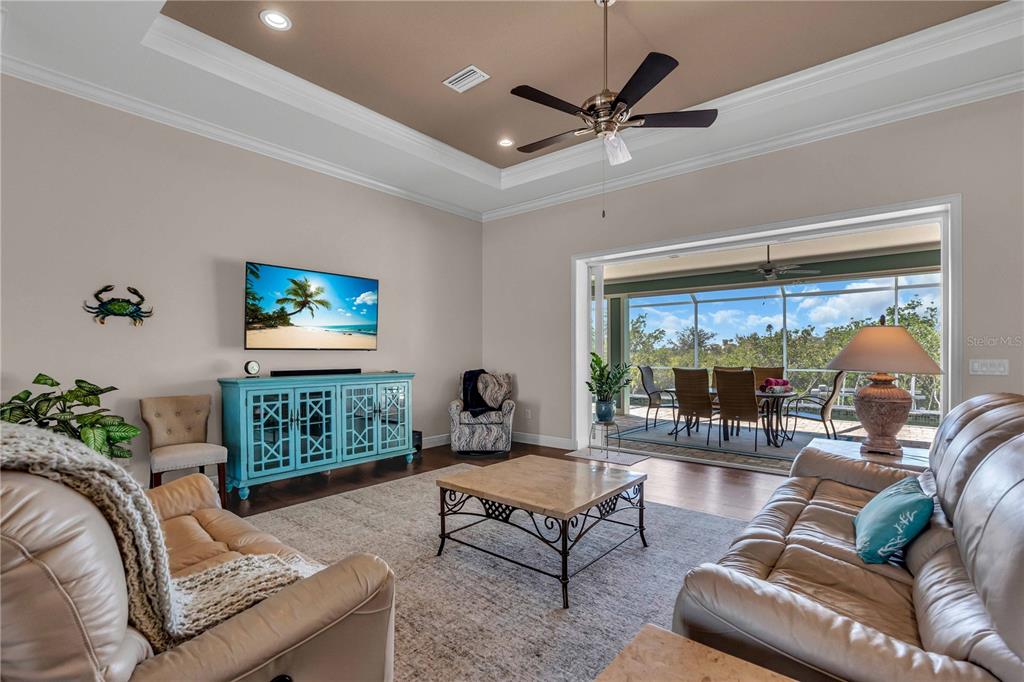 A living room features a tray ceiling, a blue media console, and sliding doors to a patio — 18091 WOODEN SKIFF COURT, NOKOMIS, FL