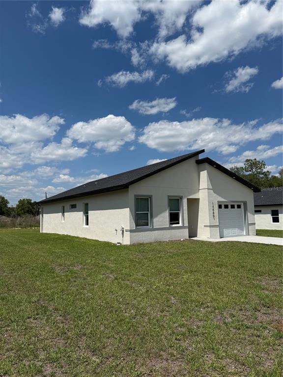 A single-story house with a stucco exterior, dark roof, and attached garage under a blue sky — 14665 SW 22ND PLACE, OCALA, FL