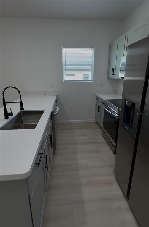 A modern kitchen features light gray cabinets, white countertops, stainless steel appliances, and wood-look flooring — 14665 SW 22ND PLACE, OCALA, FL