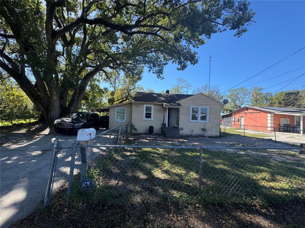 A single-story house with light siding sits behind a chain-link fence under a large tree — 1500 43RD STREET, ORLANDO, FL