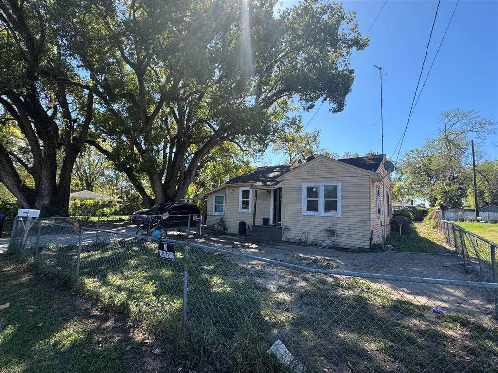 A single-story house with yellow siding sits behind a chain-link fence under large trees — 1500 43RD STREET, ORLANDO, FL
