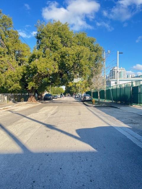 A paved street is lined with large trees, a green fence, and parked cars — 161 NW 35th St, Miami FL 33127, MIAMI, FL