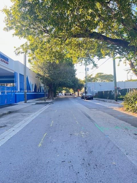 A paved street runs between a blue-trimmed building and a fenced lot under large trees — 161 NW 35th St, Miami FL 33127, MIAMI, FL