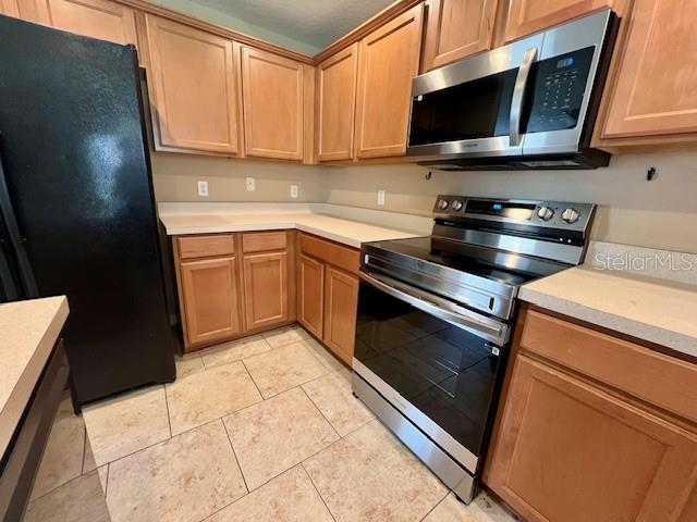 A kitchen features wood cabinets, stainless steel appliances, and light-colored tile flooring — 3522 CARUSO PLACE, OVIEDO, FL