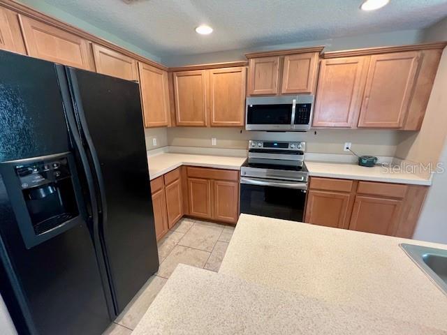 A kitchen features light wood cabinets, stainless steel appliances, and a black refrigerator — 3522 CARUSO PLACE, OVIEDO, FL