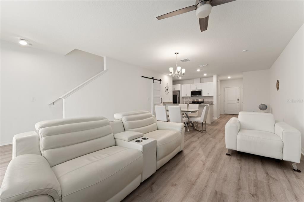 A bright, open-concept living and dining area features white leather furniture and light wood flooring — 697 STONEY POINTE CIRCLE, DAVENPORT, FL