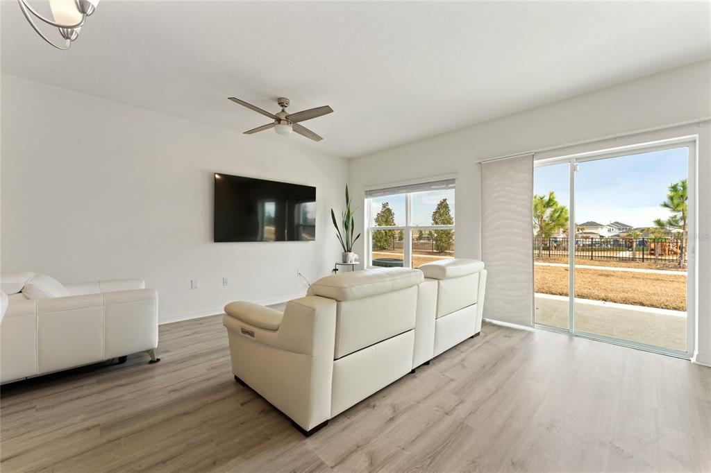 A living room features white leather sofas, a wall-mounted television, and sliding glass patio doors — 697 STONEY POINTE CIRCLE, DAVENPORT, FL