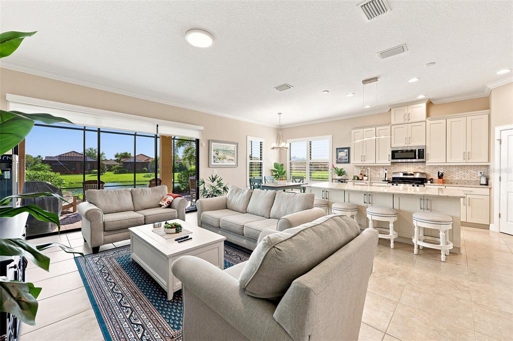 An open-concept living room and kitchen feature light-colored furniture, tile flooring, and a patio view — 4616 STICKLEY COURT, PALMETTO, FL