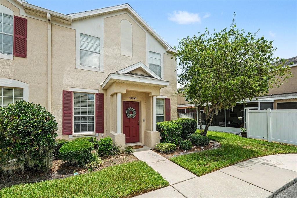 A two-story beige townhouse features a red front door, shutters, and a small front lawn — 30153 BARNABY LANE, WESLEY CHAPEL, FL