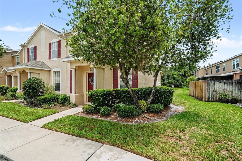 A two-story tan townhouse with red shutters, a front porch, and a landscaped yard — 30153 BARNABY LANE, WESLEY CHAPEL, FL