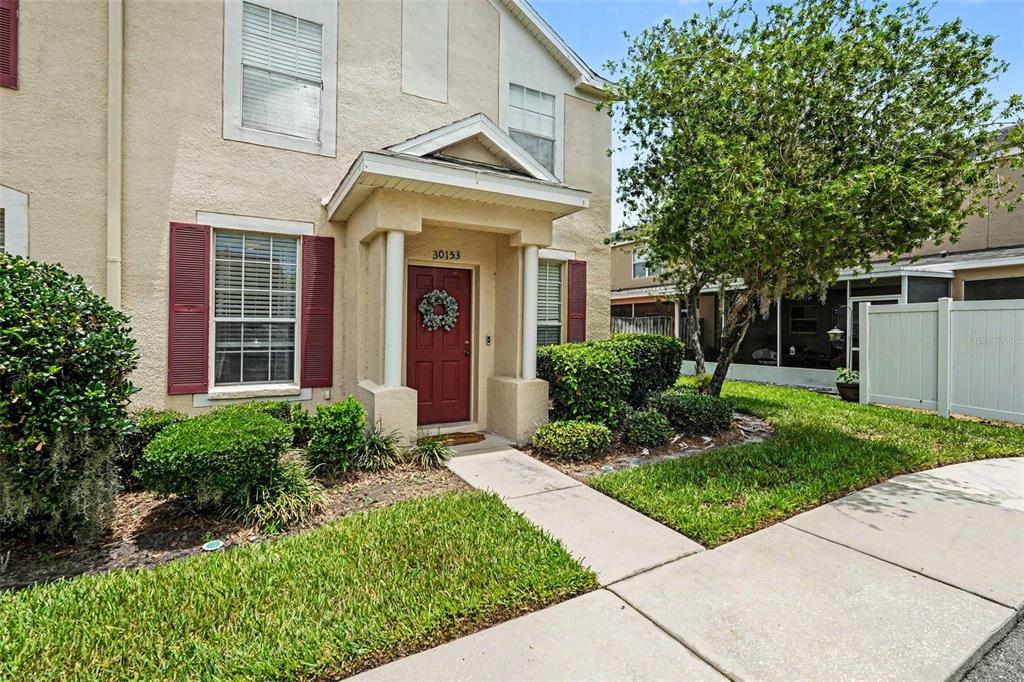 A two-story tan townhouse with a red front door and a small covered porch — 30153 BARNABY LANE, WESLEY CHAPEL, FL