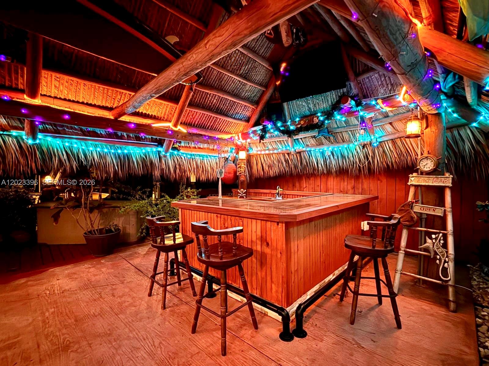 A wooden tiki bar with three stools sits under a thatched roof with colorful lights — 2730 Sherman St, Hollywood FL 33020, HOLLYWOOD, FL