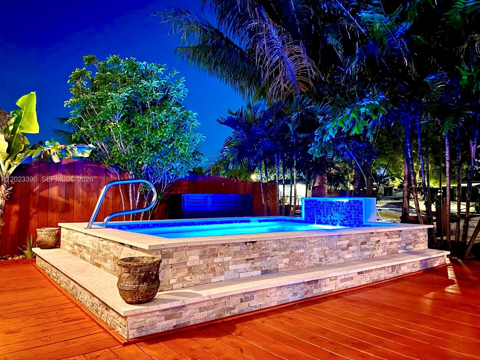 An elevated rectangular swimming pool with stone cladding sits on a wooden deck at night — 2730 Sherman St, Hollywood FL 33020, HOLLYWOOD, FL