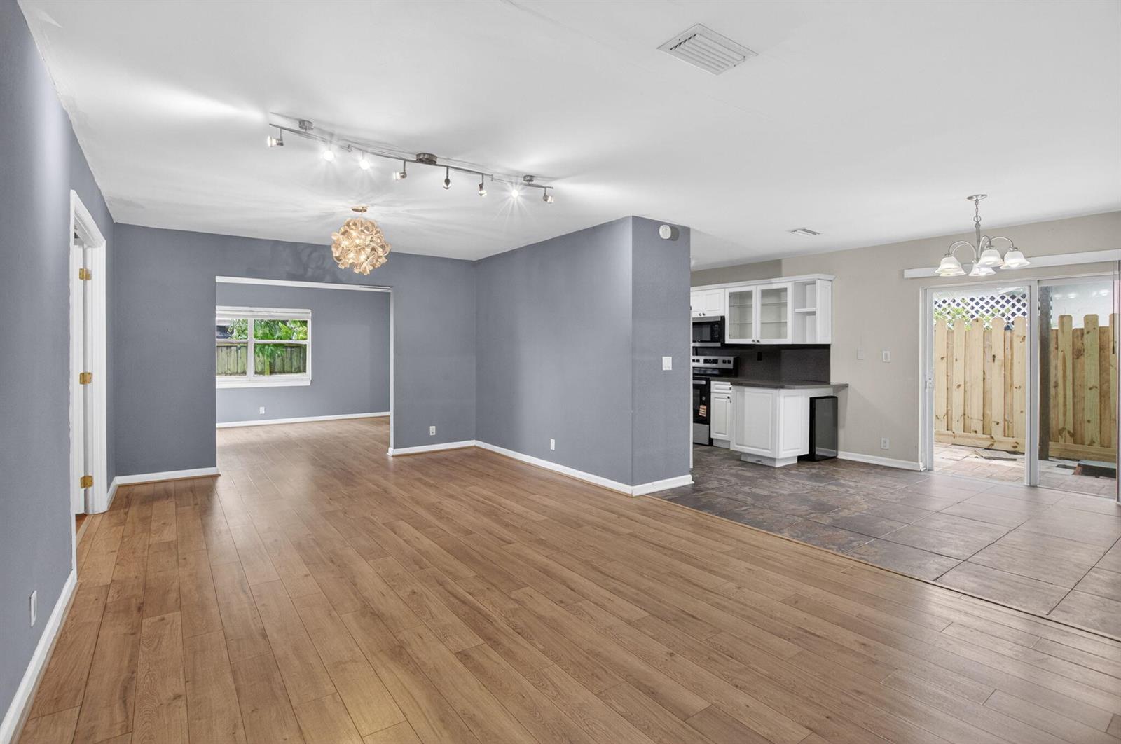 An open-concept living area features wood-look flooring, gray walls, and a tiled kitchen space — 9510 Affirmed Lane, Boca Raton FL 33496, BOCA RATON, FL