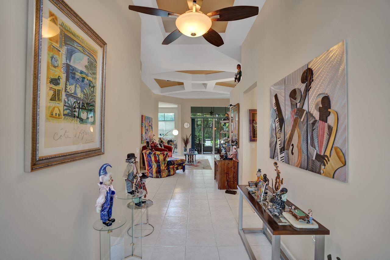 A tiled hallway leads past art-filled walls toward a living area with a ceiling fan — 1775 Annandale Circle, Royal Palm Beach FL 33411, ROYAL PALM BEACH, FL