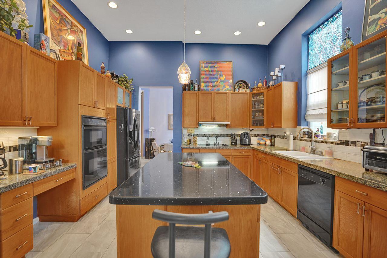 A kitchen with blue walls, wood cabinets, a black island, and light-colored tile flooring — 1775 Annandale Circle, Royal Palm Beach FL 33411, ROYAL PALM BEACH, FL