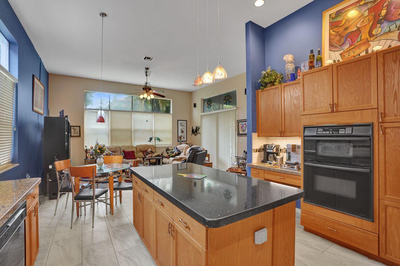 A kitchen with wood cabinets and a black island overlooks a dining and living area — 1775 Annandale Circle, Royal Palm Beach FL 33411, ROYAL PALM BEACH, FL