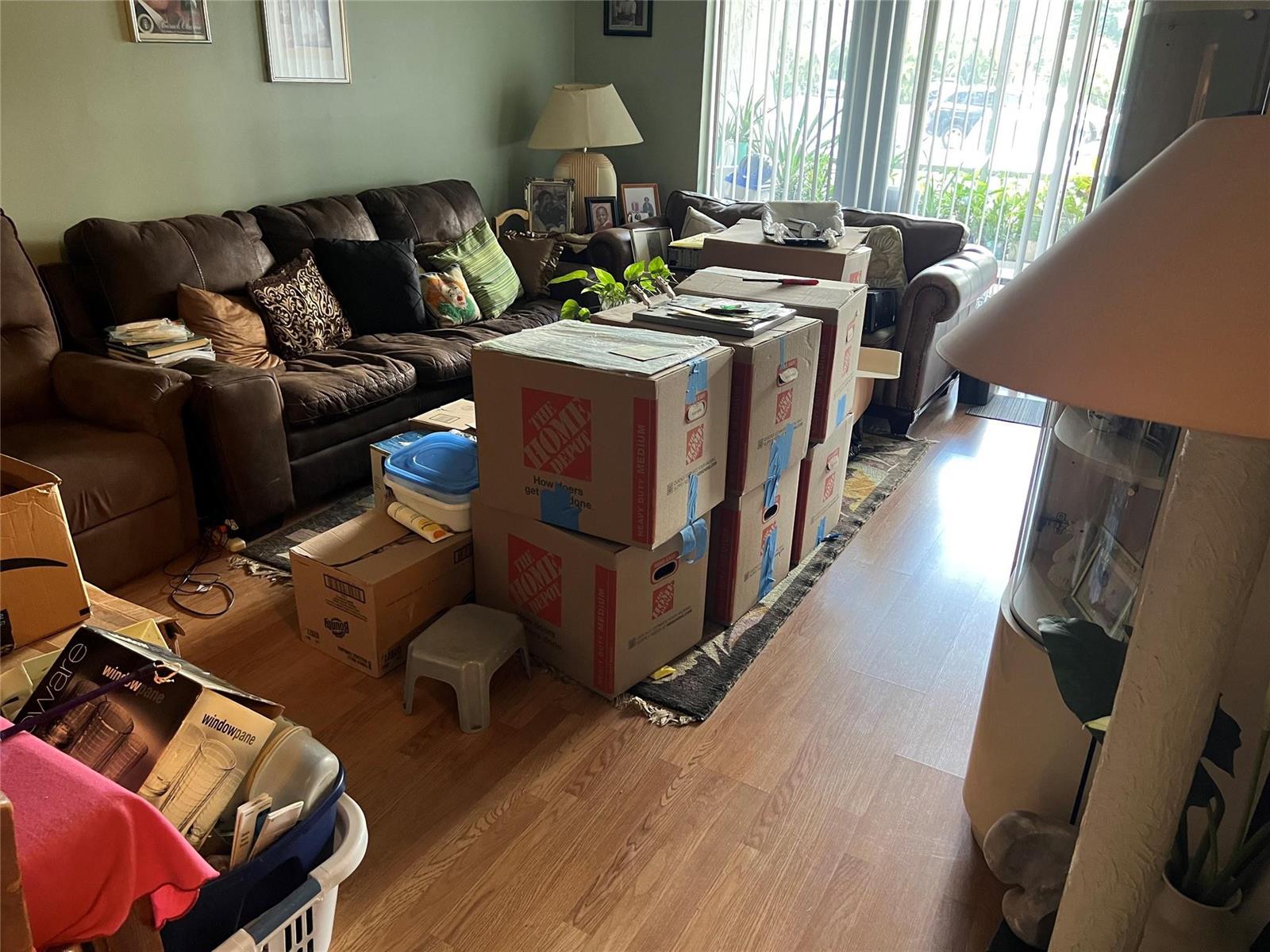 A living room with a brown sofa, wood-look flooring, and several stacked cardboard moving boxes — 3140 Holiday Springs Boulevard # 109, Margate FL 33063, MARGATE, FL