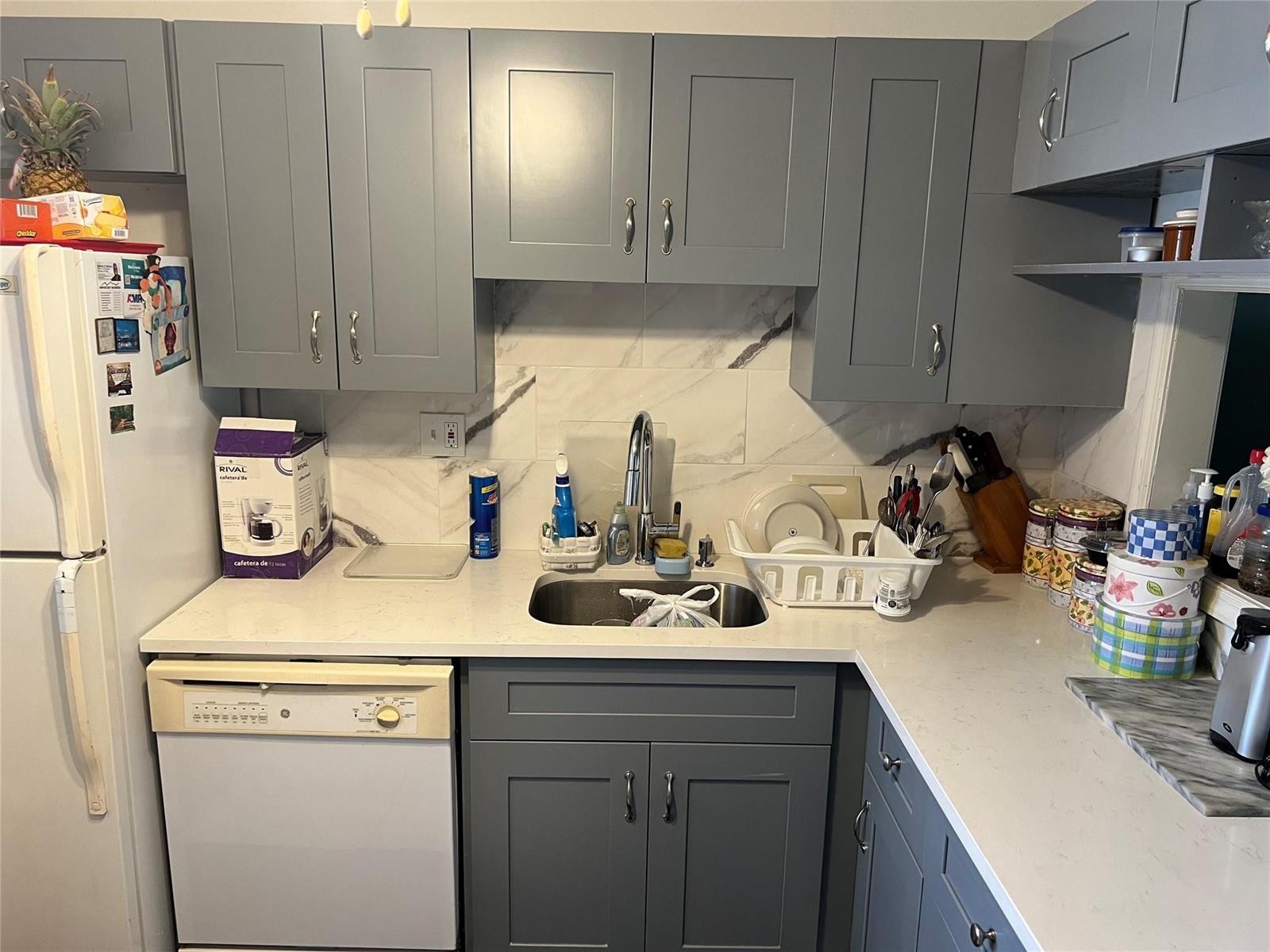 A kitchen features grey cabinets, white marble-look backsplash, white countertops, and a stainless steel sink — 3140 Holiday Springs Boulevard # 109, Margate FL 33063, MARGATE, FL