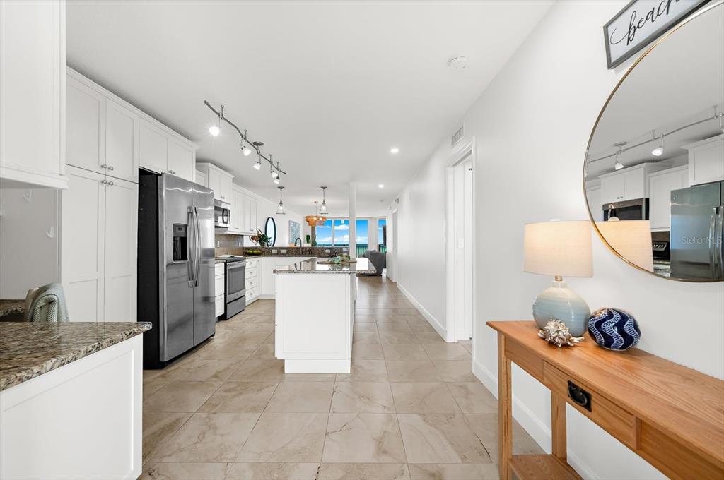 A white kitchen with stainless steel appliances and a center island overlooks a living area — 2600 GULF DRIVE N UNIT 33, BRADENTON BEACH, FL