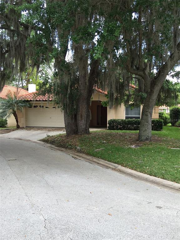 A tan house with a tile roof and a two-car garage sits behind large trees — 635 NIGHTHAWK CIRCLE, WINTER SPRINGS, FL