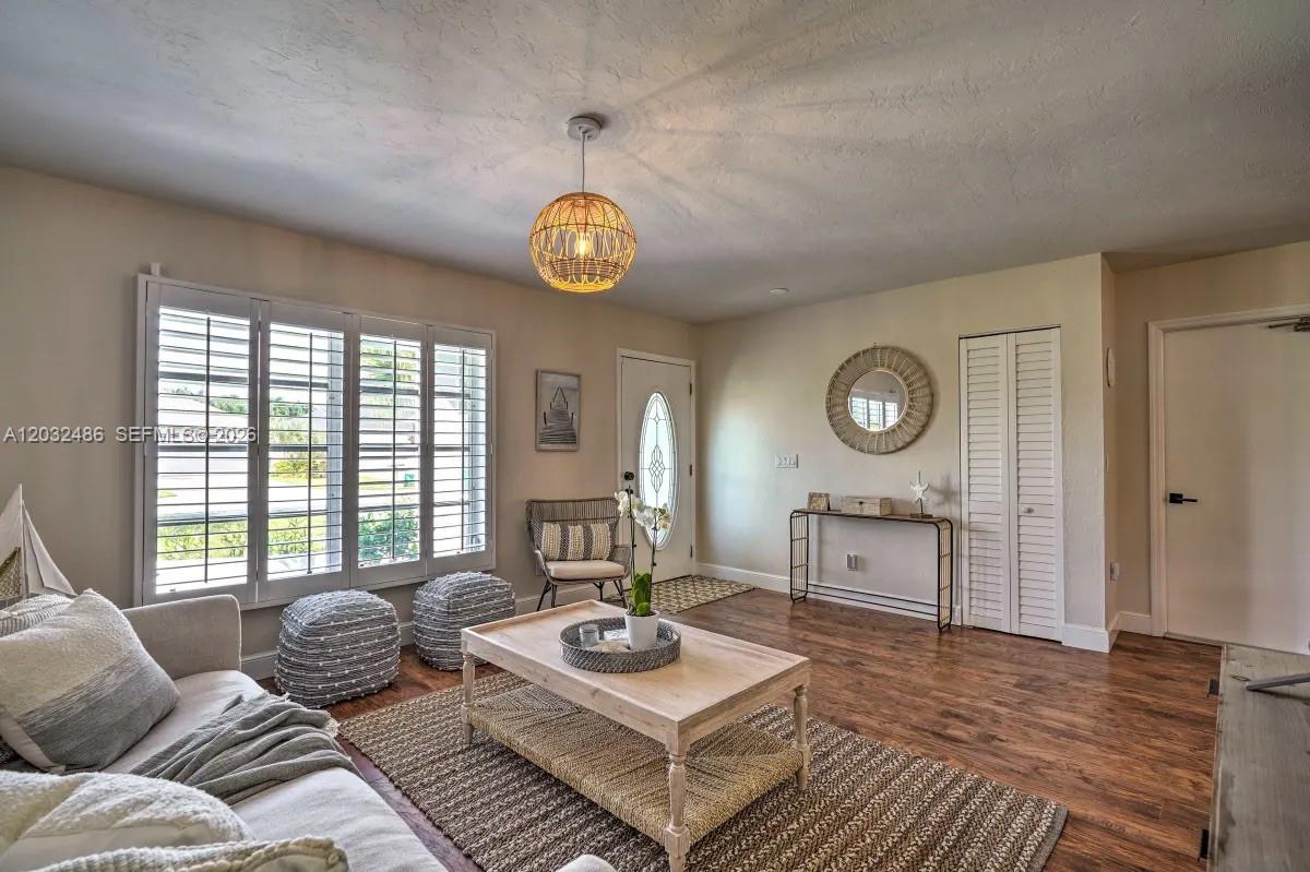 A living room features wood-look flooring, plantation shutters, a rattan pendant light, and neutral furniture — 558 102nd Ave # 0, Naples FL 34108, NAPLES, FL