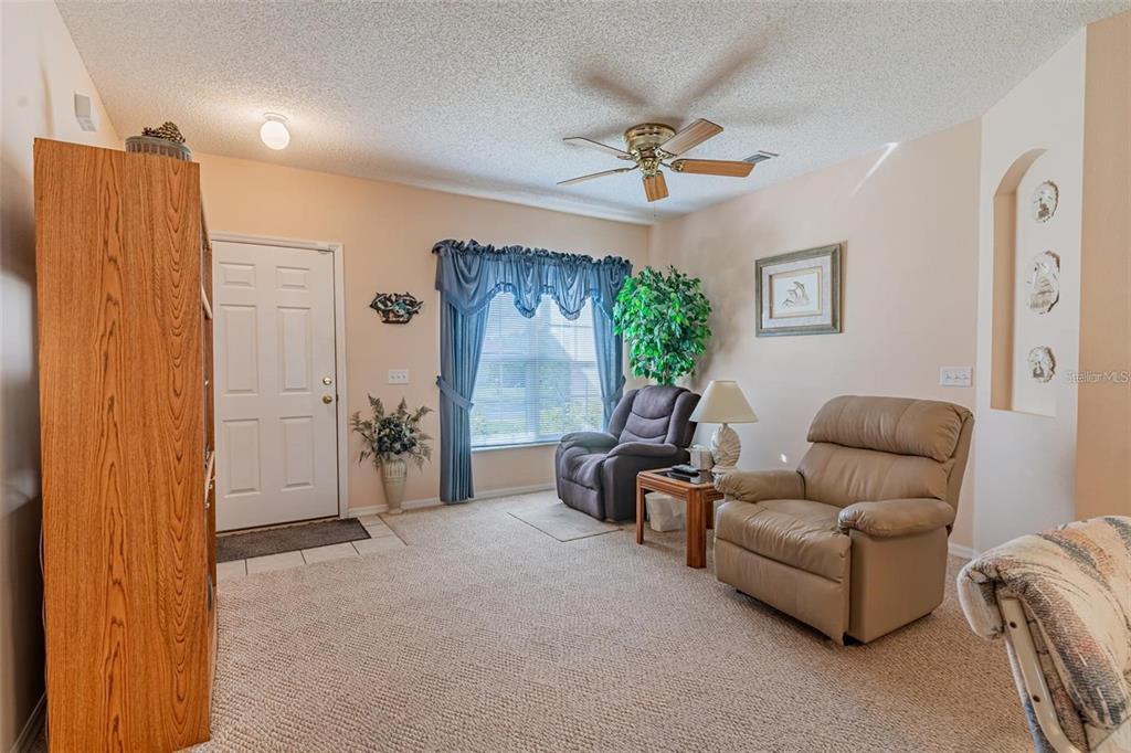 A living room features beige carpeting, two armchairs, a ceiling fan, and a front door — 7 TAMIAMI WAY, KISSIMMEE, FL