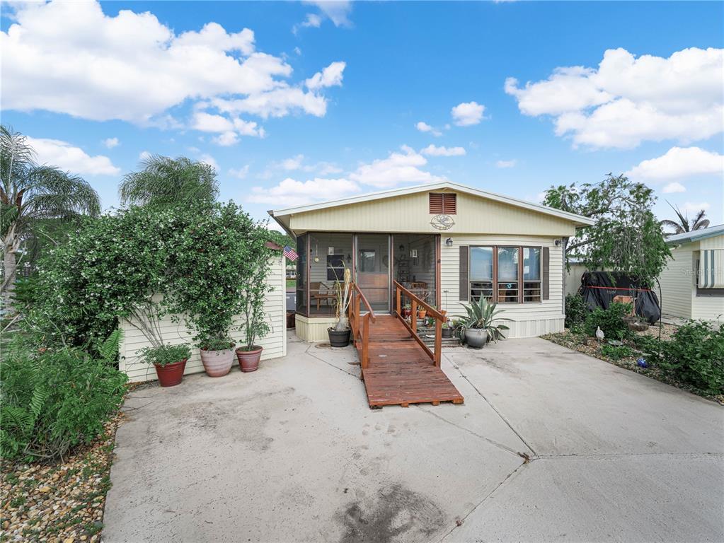 A single-story mobile home features a wooden wheelchair ramp leading to a screened front porch — 29 BEAVERKILL DRIVE, LAKE WALES, FL