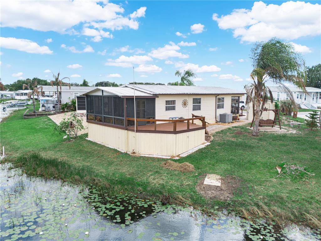 An exterior view of a mobile home with a screened porch and deck by a pond — 29 BEAVERKILL DRIVE, LAKE WALES, FL