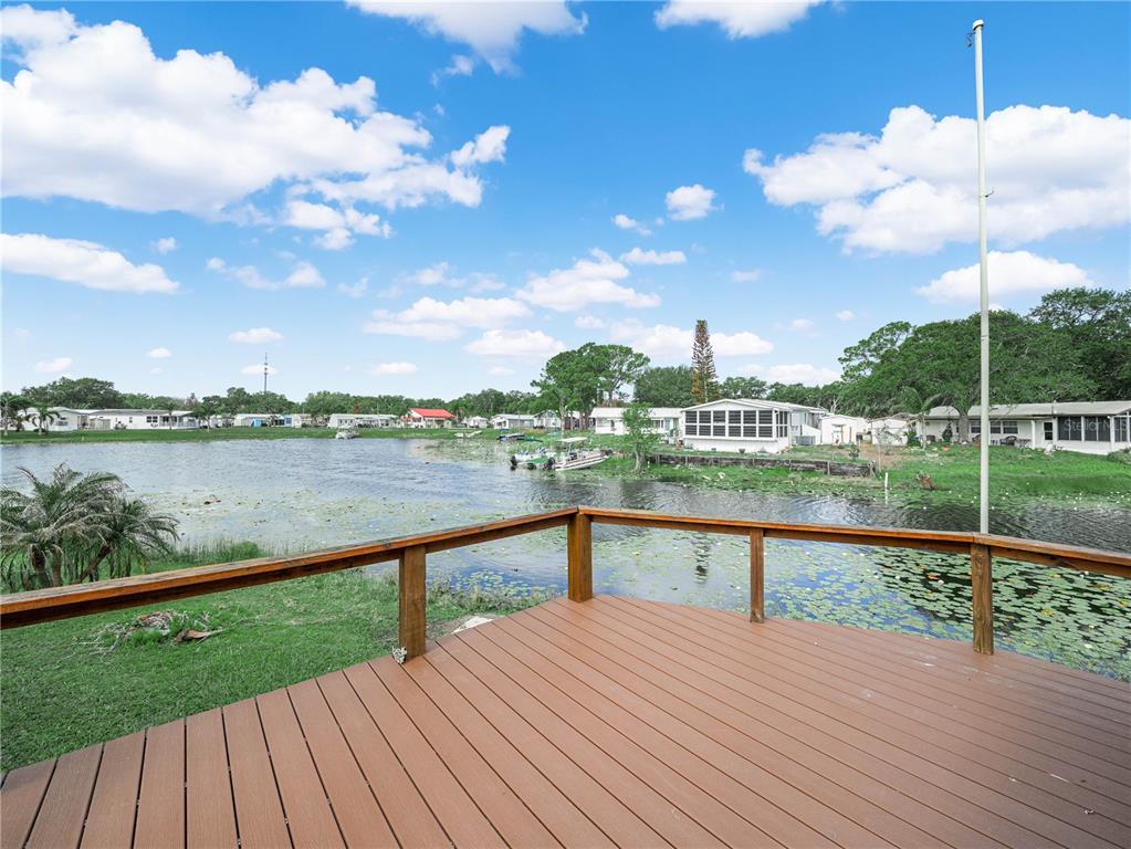 A wooden deck overlooks a pond with lily pads and houses in the distance — 29 BEAVERKILL DRIVE, LAKE WALES, FL