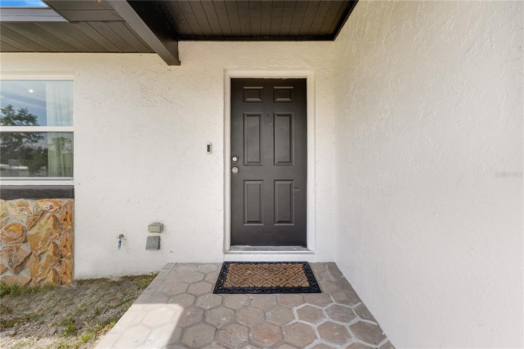 A dark front door is centered on a white stucco wall above a stone patio — 712 OAK LANE, GROVELAND, FL