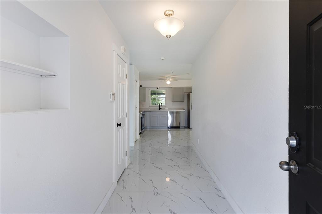 A hallway with white marble-look tile floors leads to a kitchen with gray cabinets — 712 OAK LANE, GROVELAND, FL