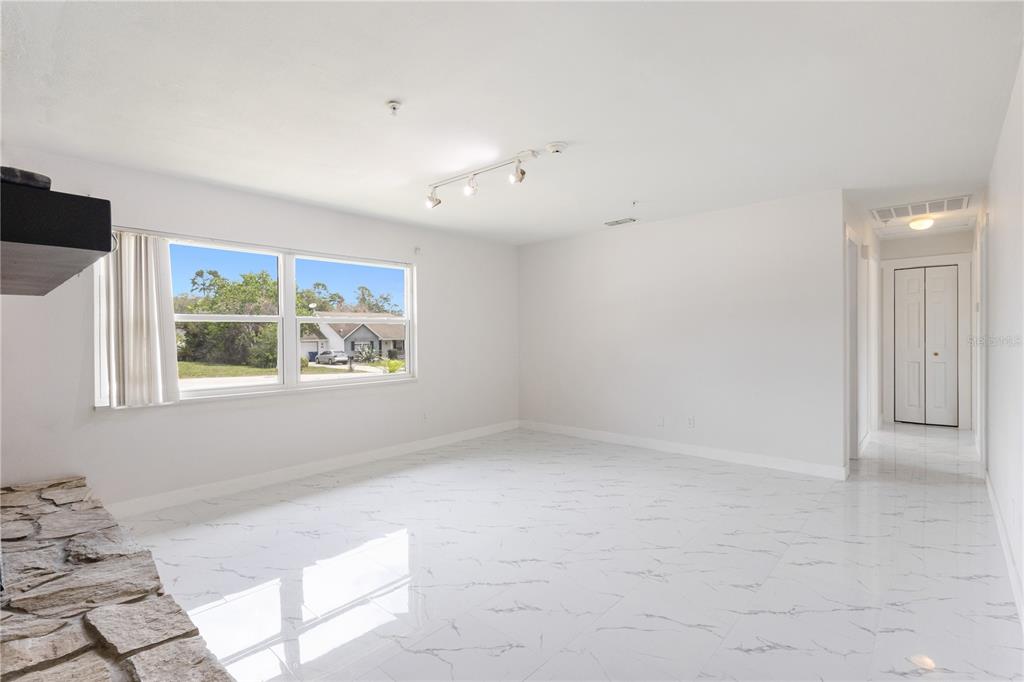 A bright, empty living room features white marble-look tile flooring and a stone fireplace hearth — 712 OAK LANE, GROVELAND, FL
