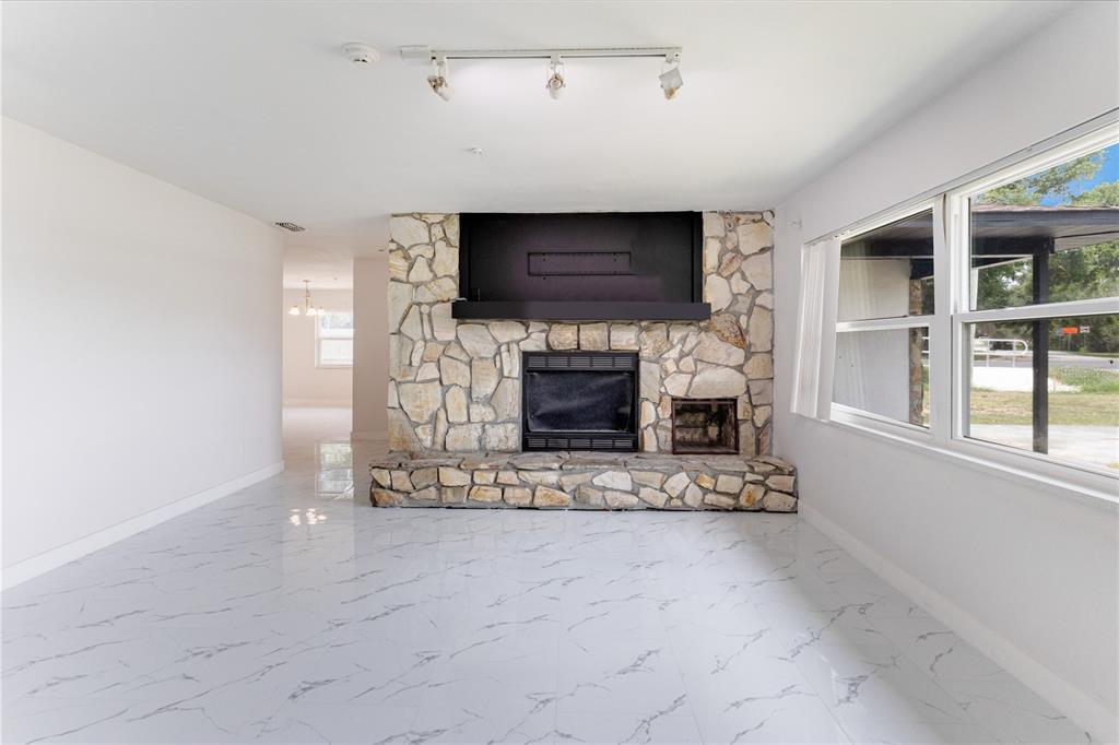 A living room features white marble-look tile flooring and a large stone fireplace with hearth — 712 OAK LANE, GROVELAND, FL