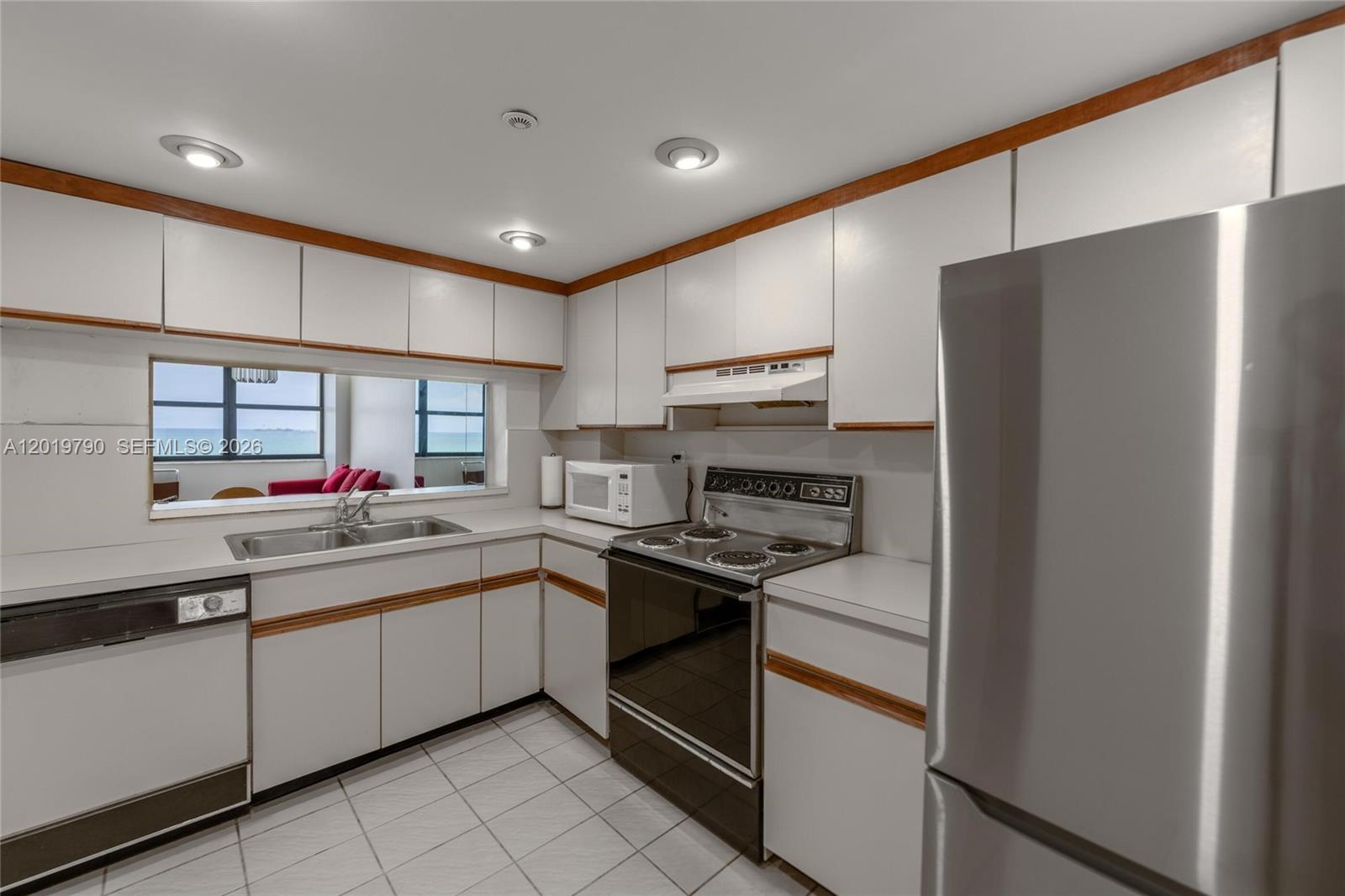A kitchen features white cabinets with wood trim, stainless steel appliances, and a pass-through window — 2555 Collins Ave # 1003, Miami Beach FL 33140, MIAMI BEACH, FL