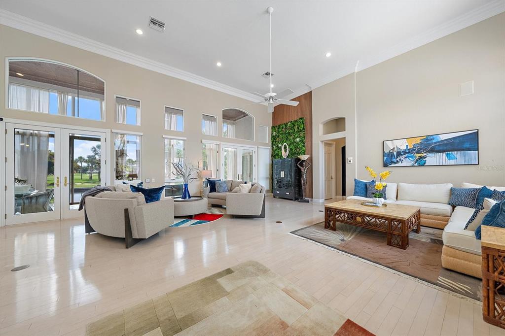 A spacious living room with high ceilings, light wood floors, and large windows overlooking outdoors — 617 WESTON POINTE COURT, LONGBOAT KEY, FL