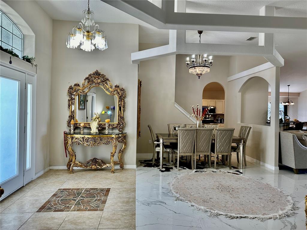 An entryway with a gold console table and mirror leads into a dining room area — 1947 FAIRWAY LOOP, KISSIMMEE, FL