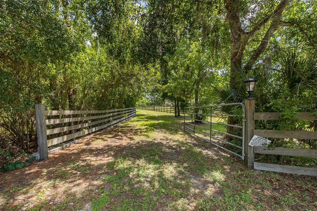A gated entrance with a wooden fence leads to a dirt path through a wooded area — 0 TRACKSIDE DRIVE, ODESSA, FL