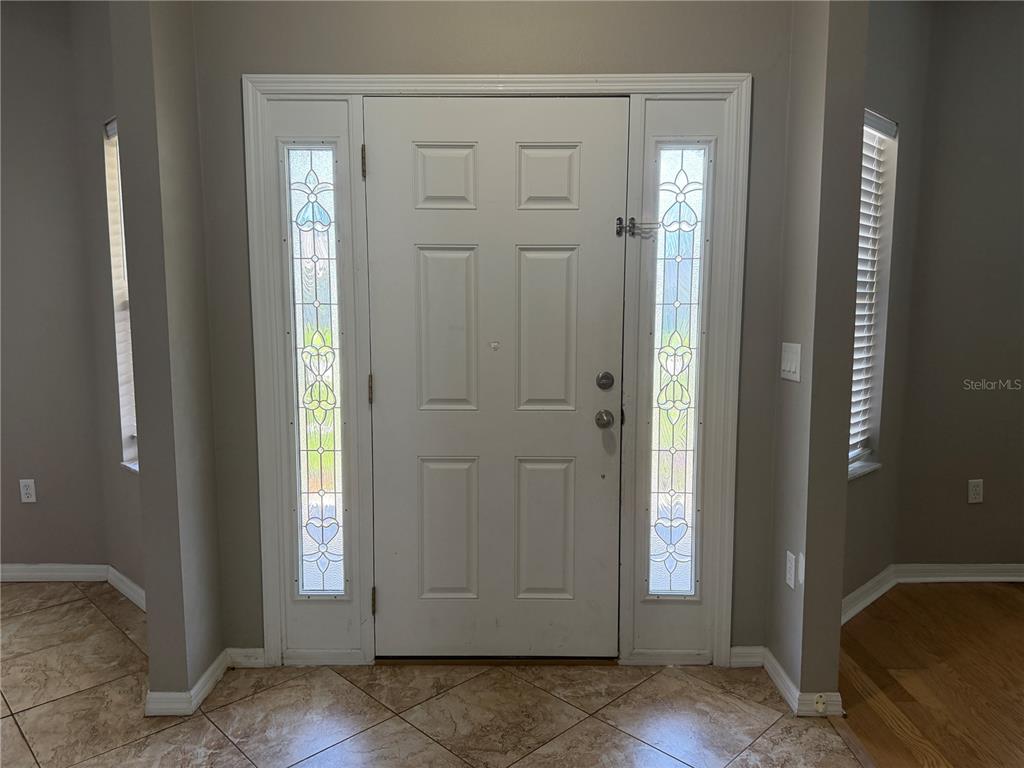 A white front door with glass sidelights is centered in a neutral-walled entryway with tile flooring — 29 FORSYTHE LANE, PALM COAST, FL