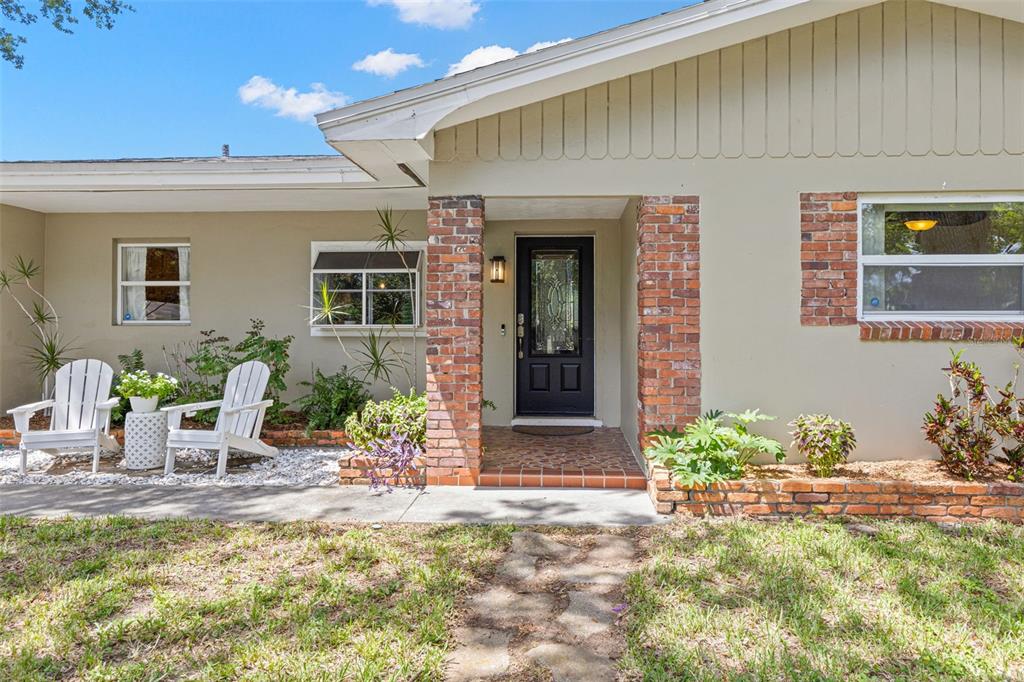 A single-story house exterior features a brick-columned entryway, white Adirondack chairs, and a front lawn — 1950 REBECCA DRIVE, CLEARWATER, FL