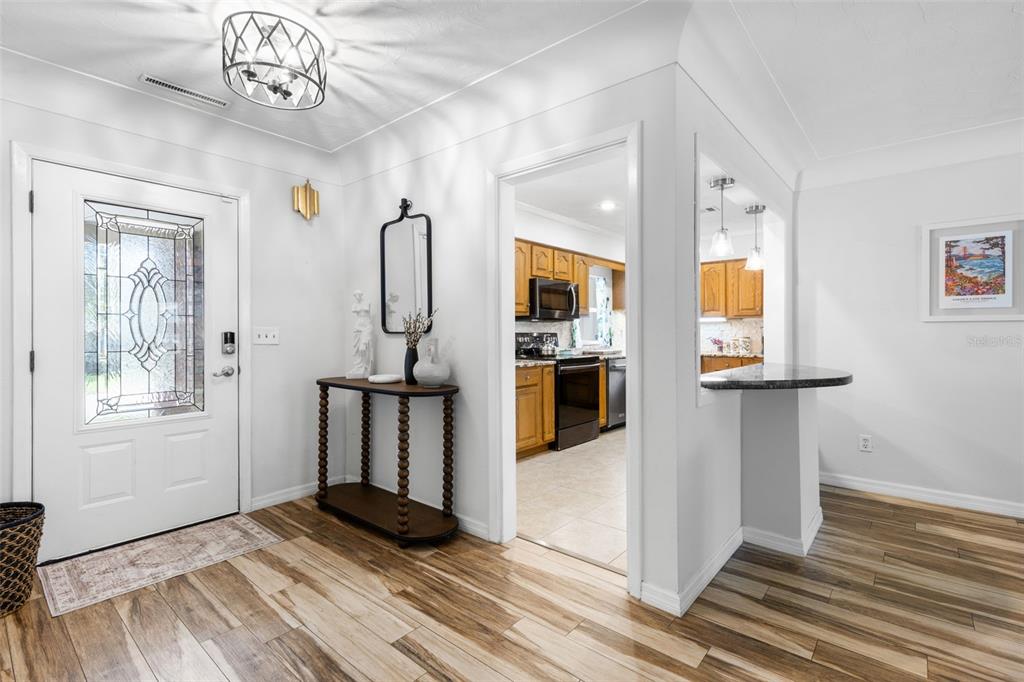 An entryway with wood-look tile flooring leads to a kitchen through an open doorway — 1950 REBECCA DRIVE, CLEARWATER, FL